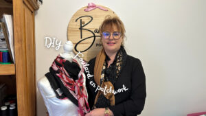 femme habillée en noir qui porte des lunettes qui pose à côté d'un mannequin en bois avec un foulard dessus
